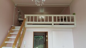 A room with a bunk bed, a wooden ladder, a chandelier, and a door with a window. - Dreaming Forest (Seogwipo)
