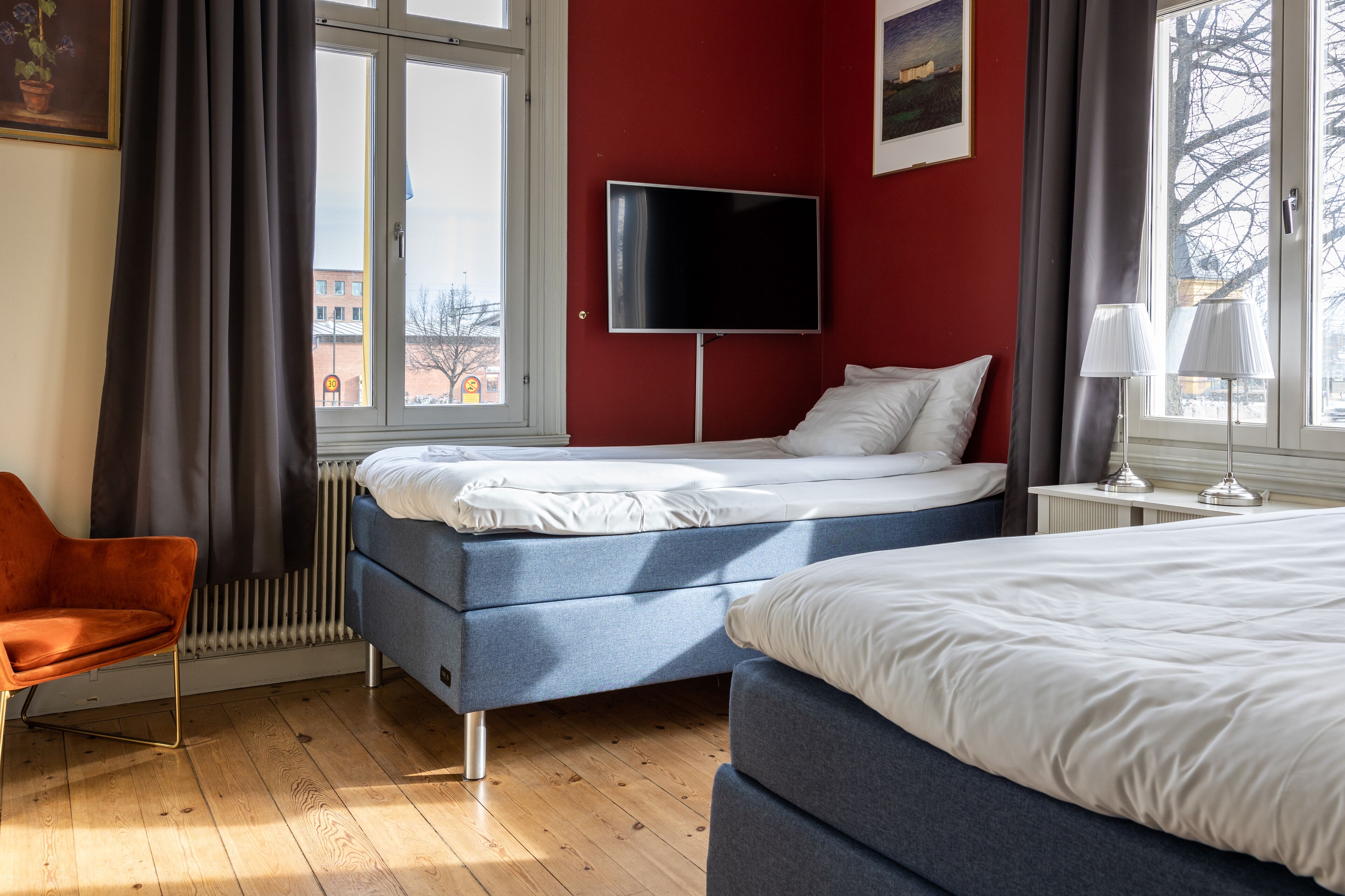 A hotel room with a bed, a chair, a TV, and a window with curtains.
