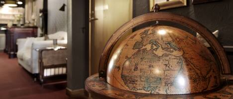 A globe on a wooden stand in a room with framed pictures on the wall and a sofa in the background.