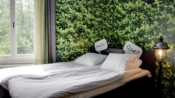 Un dormitorio con cama, ventana, pared con follaje verde y lámpara.