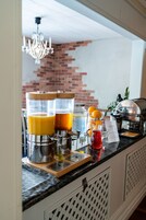 Una barra de desayuno con cafetera, dispensadores de jugo y una jarra roja para bebidas.
