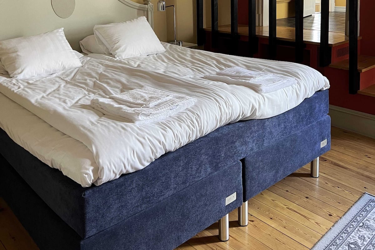 Una cama bien hecha con sábanas blancas, un cabecero con un panel decorativo y un suelo de madera.