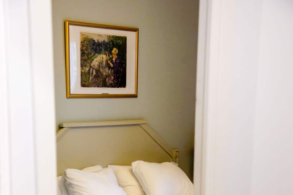 Un baño con cama, un cuadro enmarcado en la pared y una planta al frente.