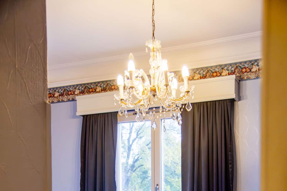Un dormitorio con cama, ventana con cortinas, radiador y candelabro.