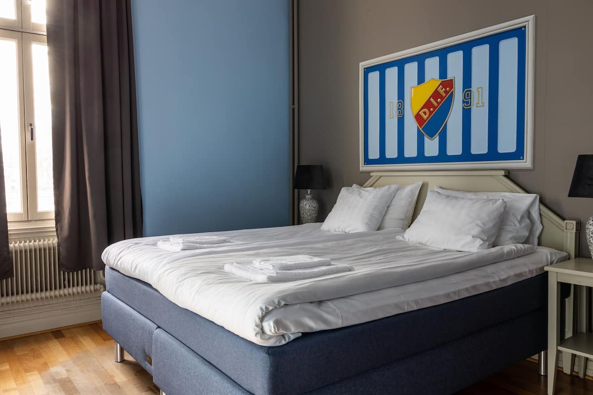 Una cama bien hecha con sábanas blancas, un cabecero azul y un logotipo de equipo deportivo colgado en la pared.
