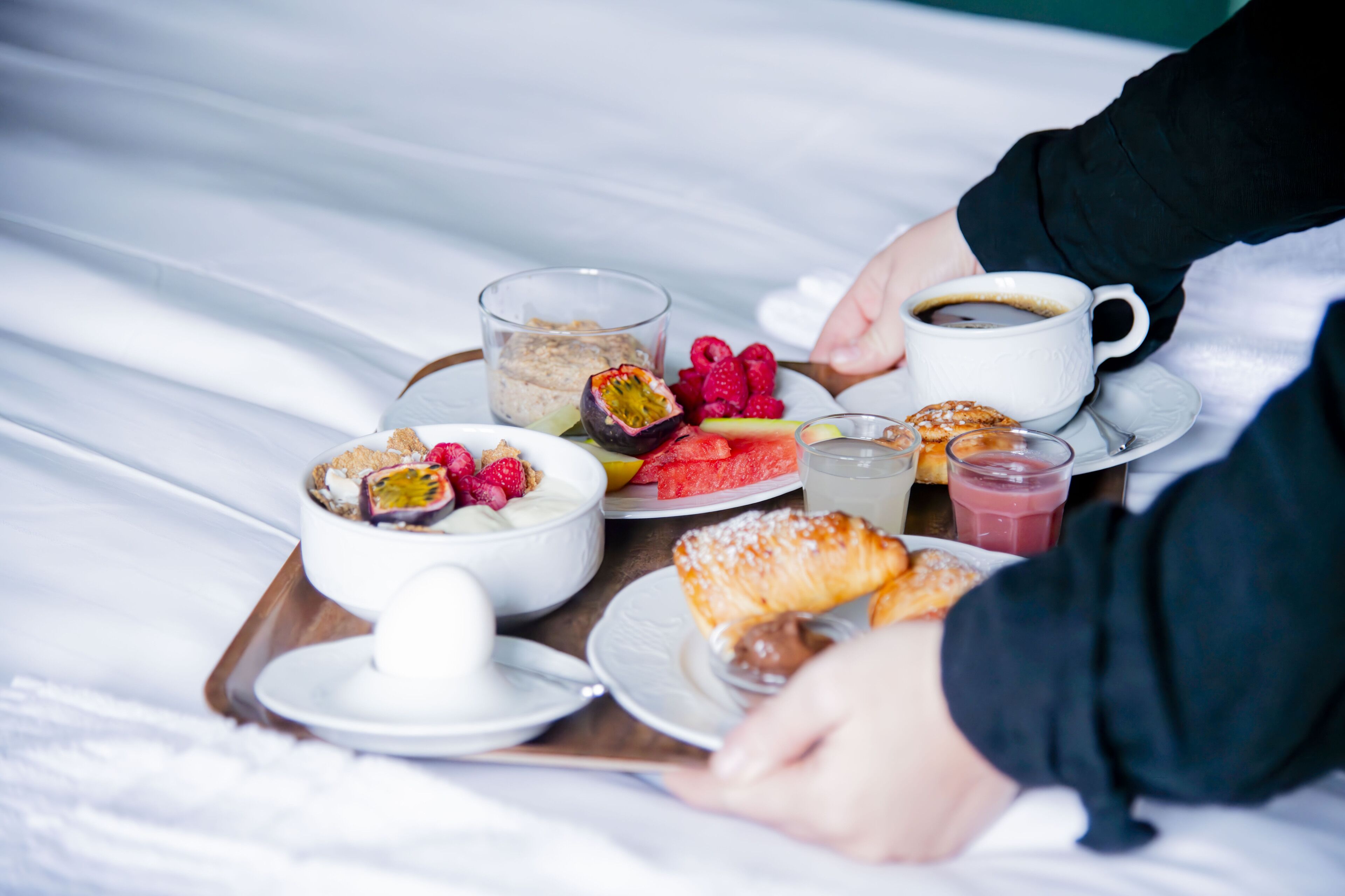 A breakfast tray with various foods and drinks on a bed.