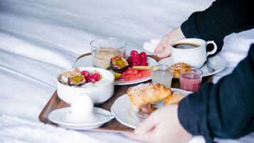 A breakfast tray with various foods and drinks on a bed.