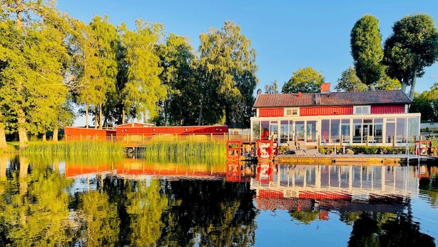 Un bâtiment situé au bord de la rivière, avec une façade rouge et blanche qui se reflète dans l’eau calme.