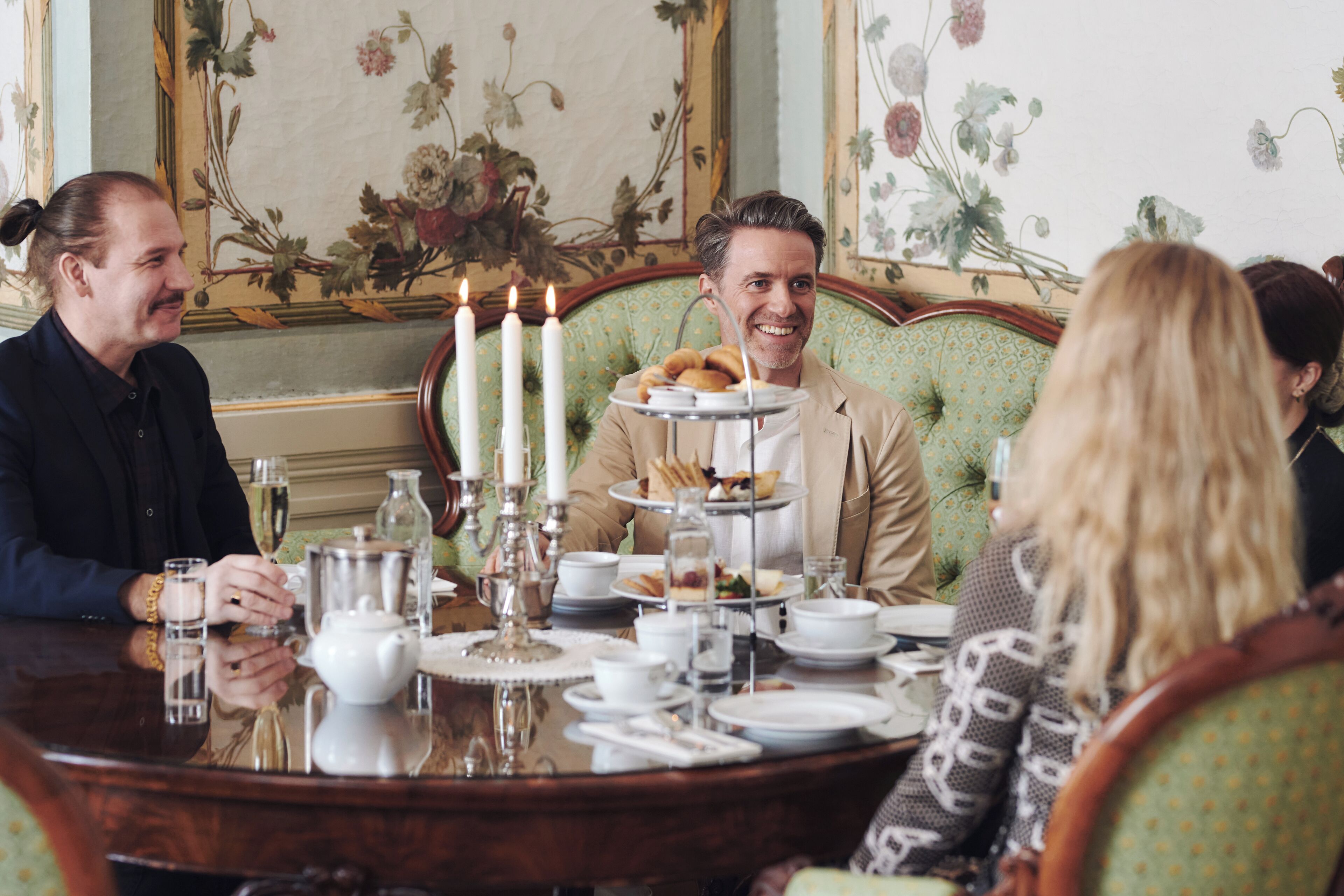 Un ambiente de comedor formal con un pastel de tres pisos, velas y un fondo de papel tapiz con motivos florales.
