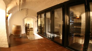 Un couloir avec une barrique en bois, un sol carrelé et des portes vitrées donnant sur une cave à vin.