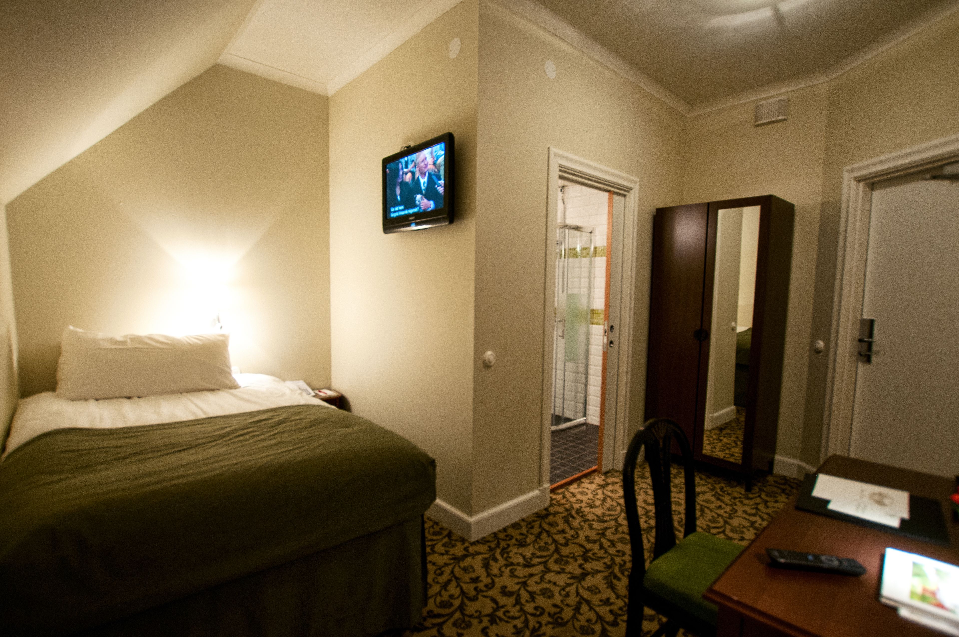 Een hotelkamer met een bed, een aan de muur bevestigde televisie, een bureau met een afstandsbediening en een spiegel.