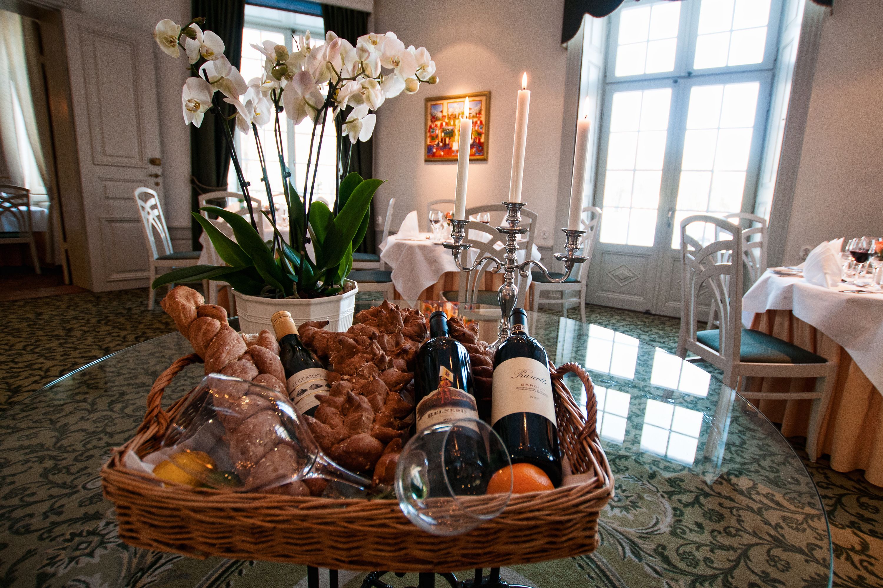 A dining area with a table set for a meal, featuring a basket of bread, wine bottles, and a potted plant.