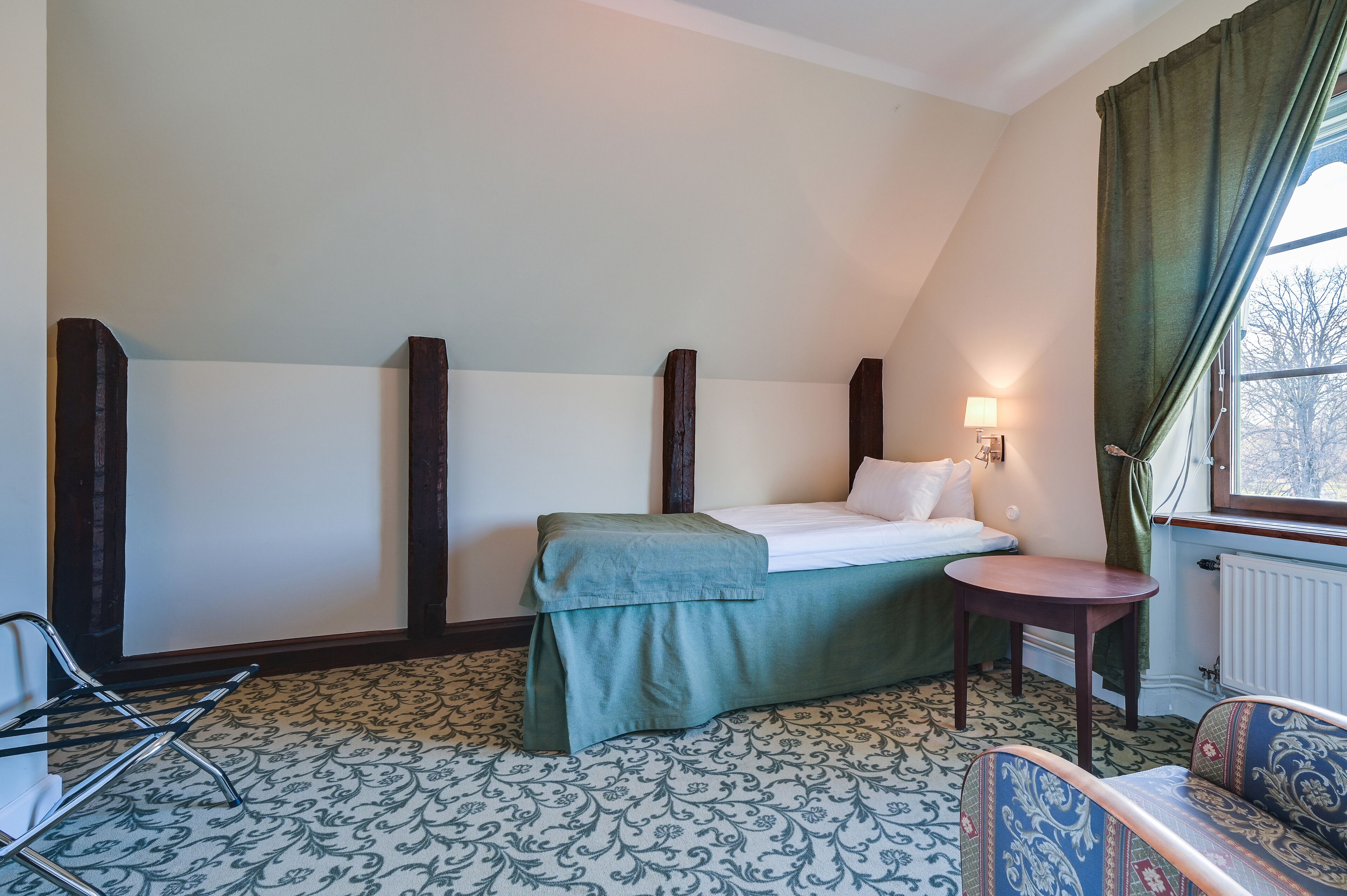 A room with a bed, a small table, a chair, and a window with curtains.