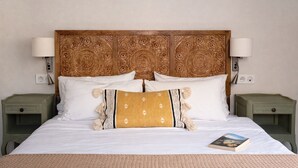 Cama com cabeceira de madeira, roupa de cama branca e duas mesas de cabeceira com abajures.