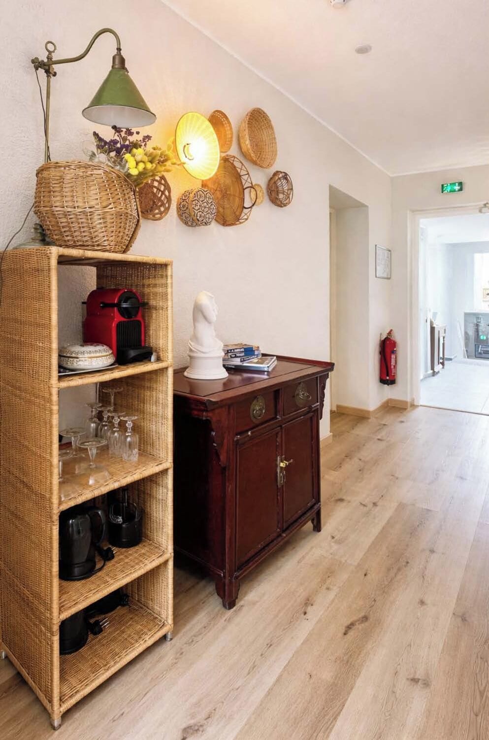 A room with a wicker shelf unit, a wooden cabinet, and a wall-mounted lamp.