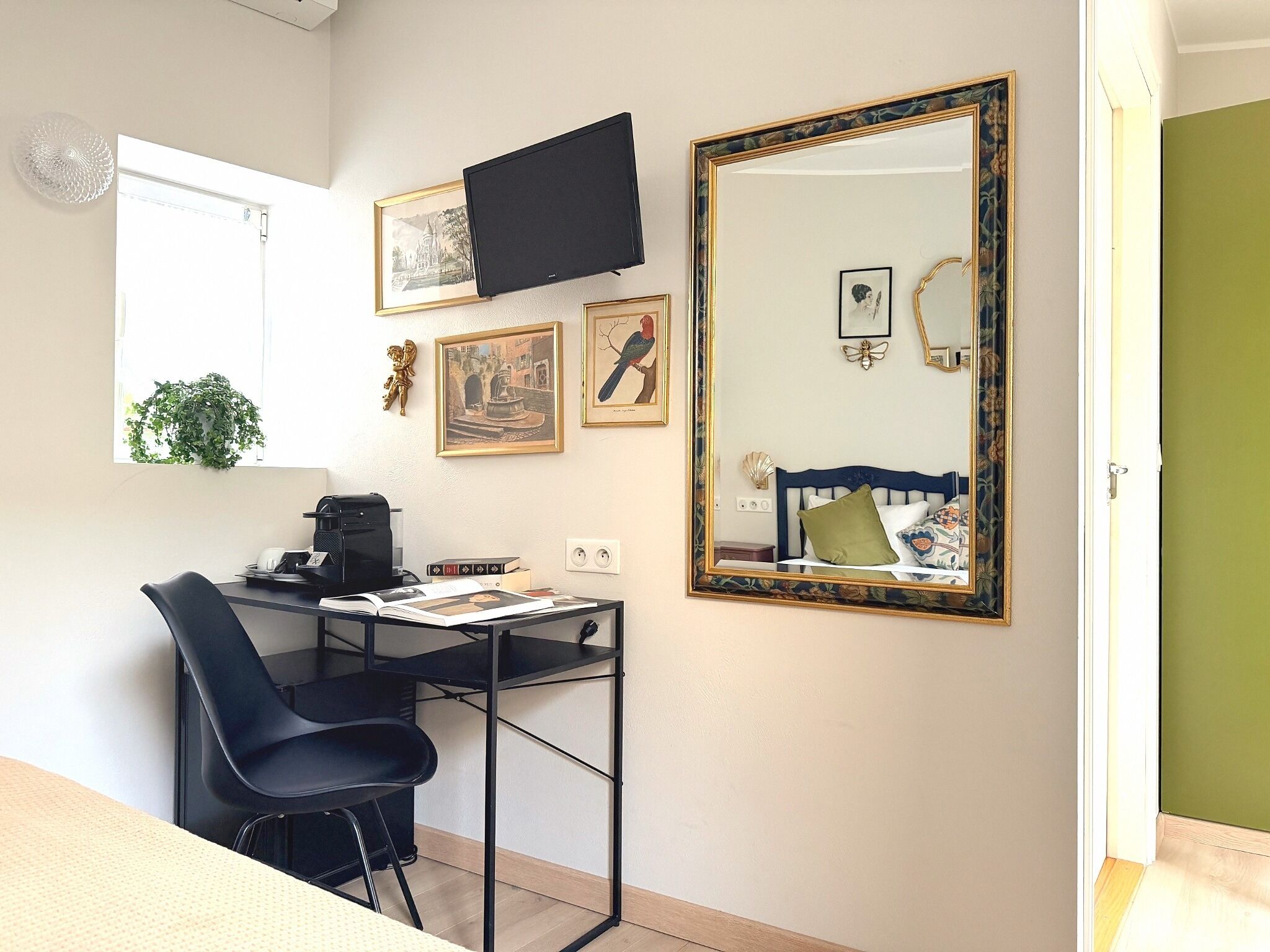 Un dormitorio acogedor con una cama, un escritorio con silla, un espejo grande y varias fotografías enmarcadas en la pared.