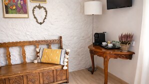 Um quarto acolhedor com um banco de madeira, uma pequena mesa com abajur e televisão na parede.