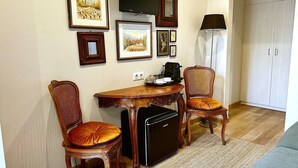 Quarto compacto com mesa de jantar, duas cadeiras, máquina de café, televisão e quadros na parede.