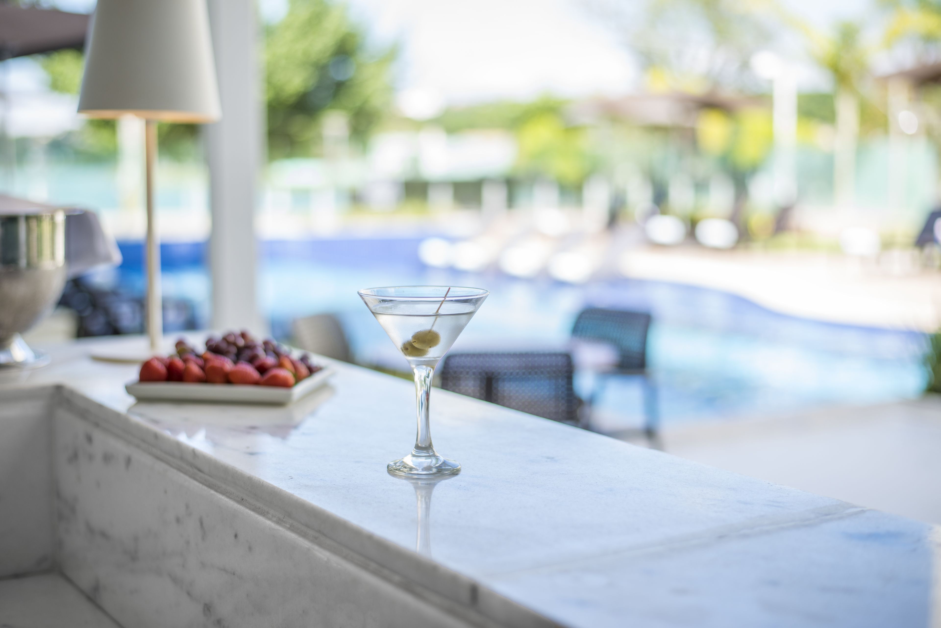Duidelijk uitzicht op een zwembad met ligbedden en een tafel met een martini en fruit.