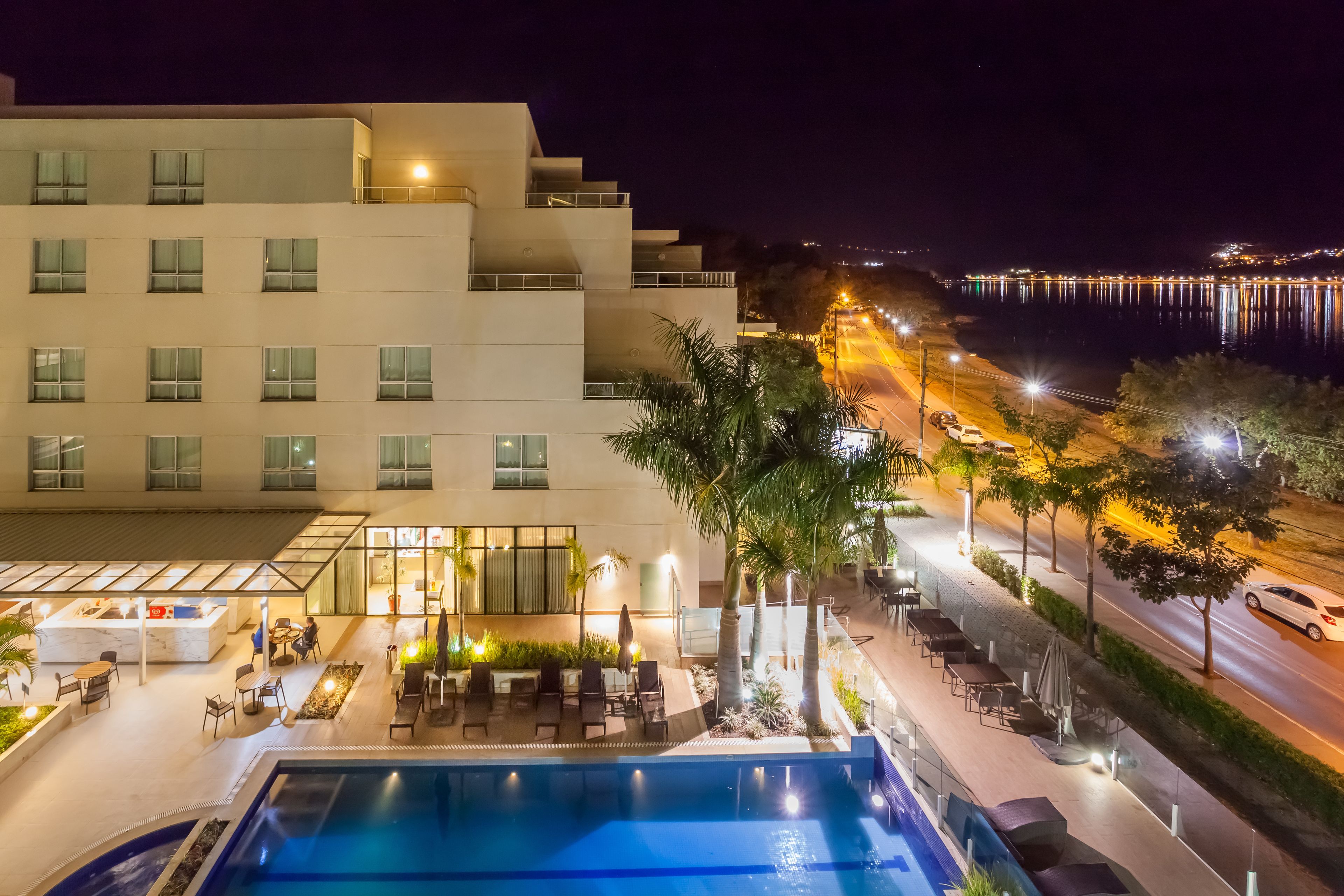 A hotel with a pool, outdoor seating, and a view of the waterfront at night.