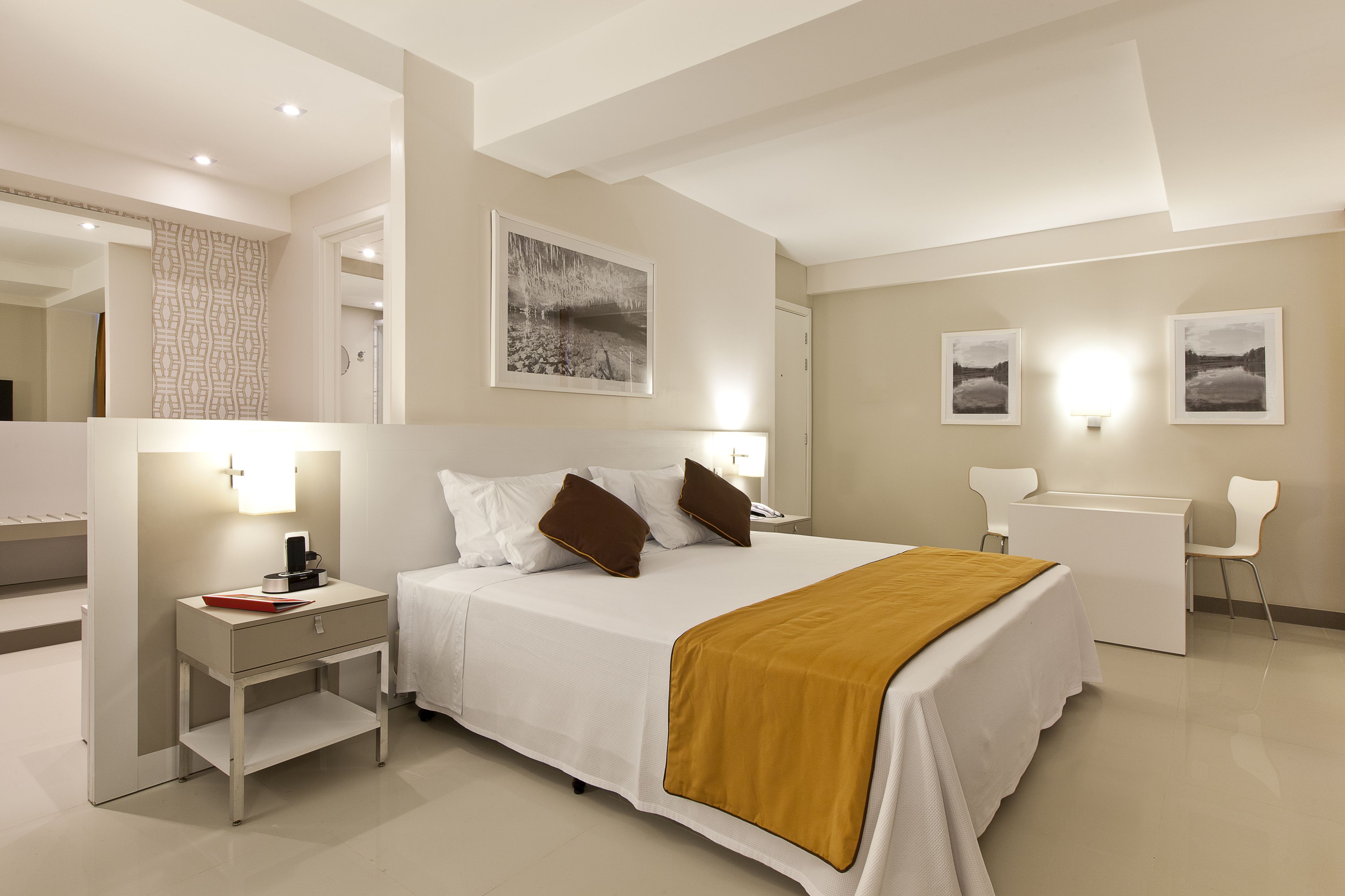 Quarto de hotel moderno com uma cama grande, mesas de cabeceira, uma escrivaninha e uma cadeira.
