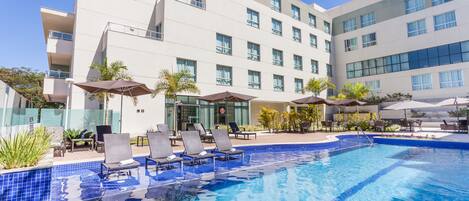A modern hotel with a swimming pool, lounge chairs, and umbrellas.