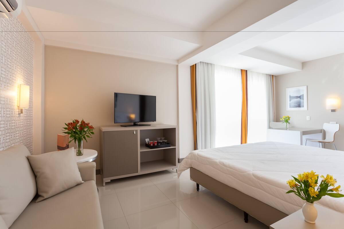 A modern hotel room with a bed, a TV, a desk, and a sofa.