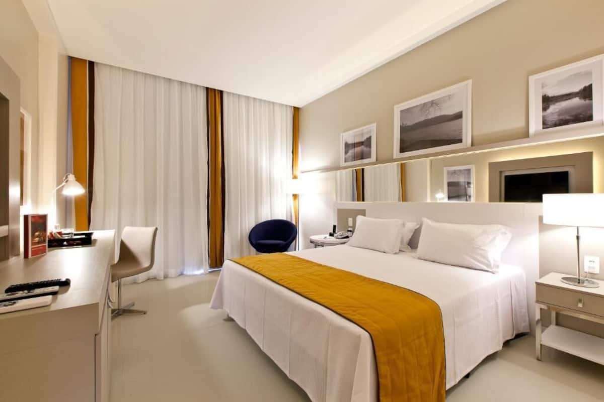 A hotel room with a bed, a desk, a chair, a bedside table, and a TV.