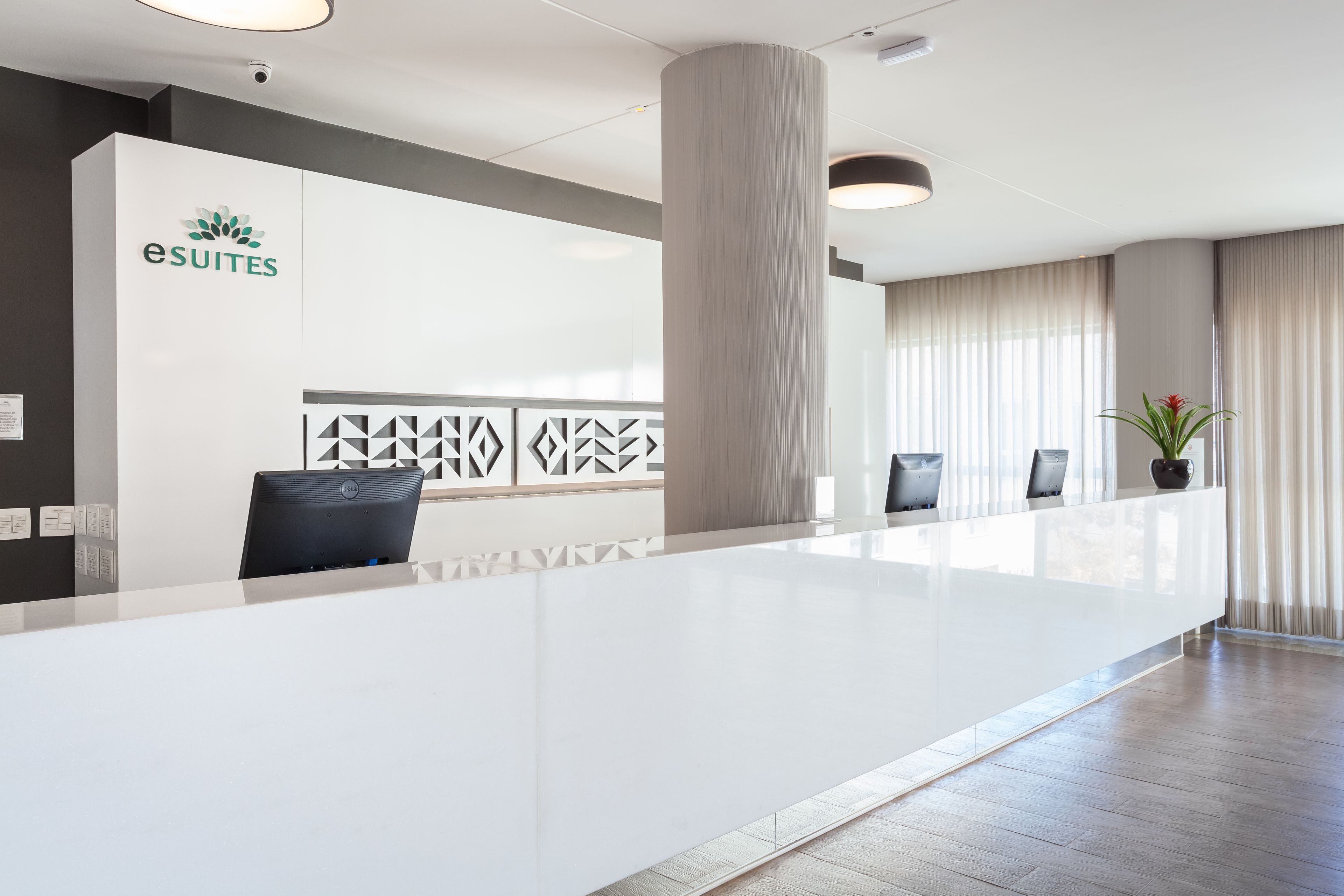 Un área de recepción moderna con un mostrador blanco, el logotipo de 'eSuites' y una pared con diseño.