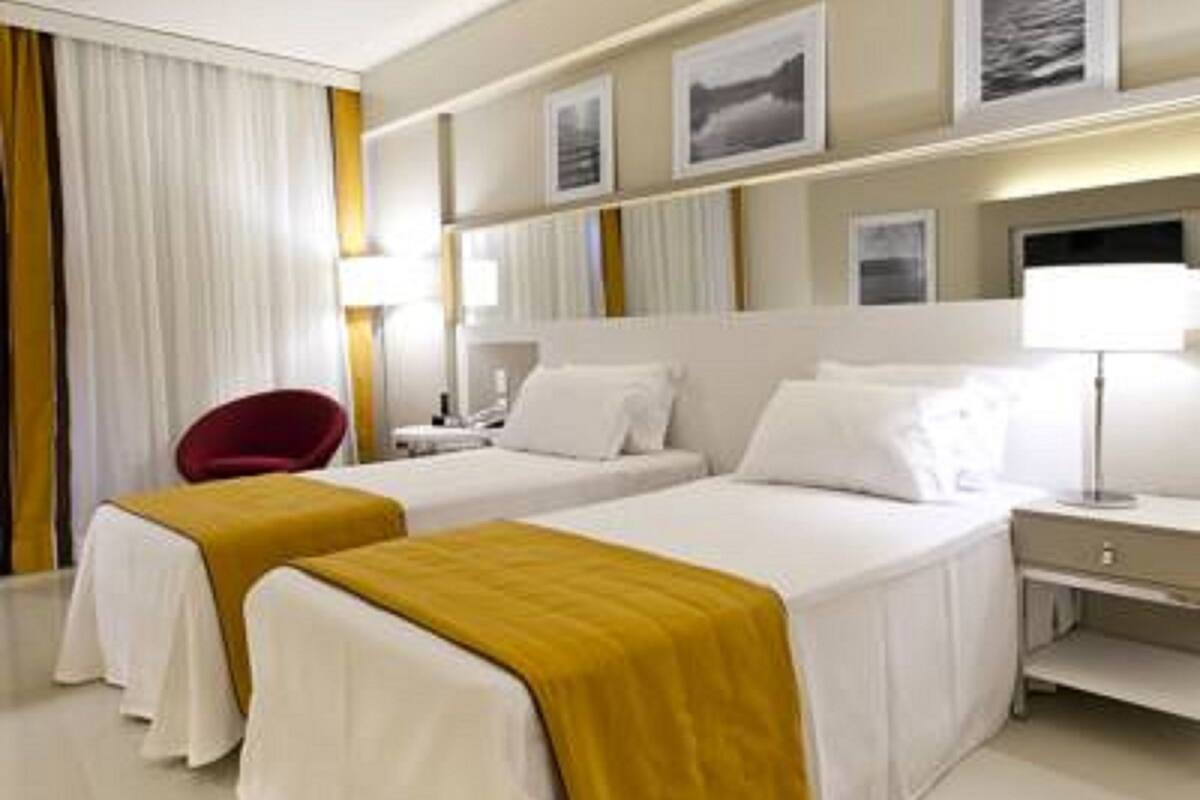 A hotel room with two beds, a red chair, a desk, and a nightstand.