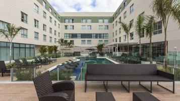 A modern hotel courtyard with a swimming pool, lounge chairs, and a seating area.