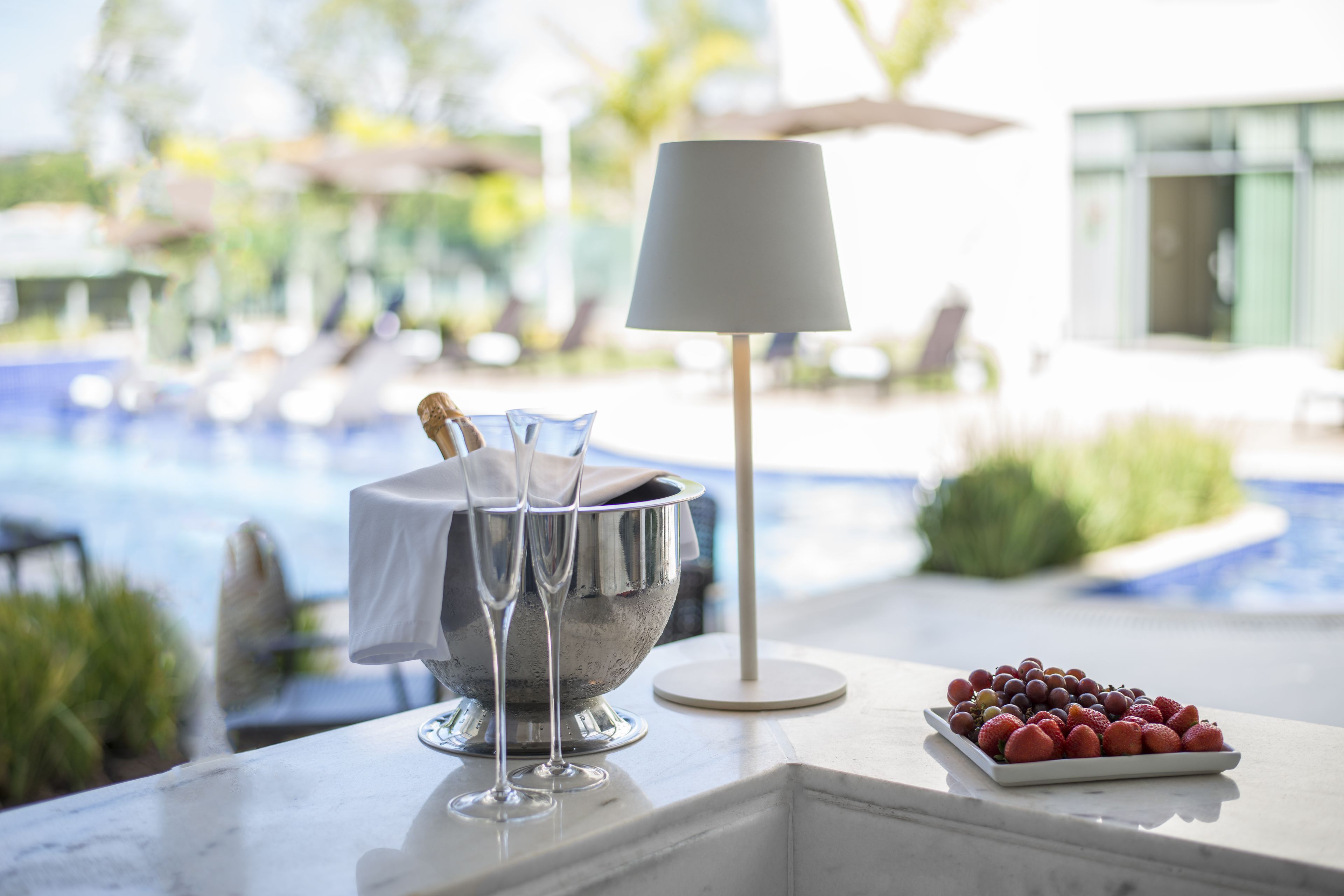 Ambiente à beira da piscina, com balde de champanhe, copos e uma bandeja de frutas.