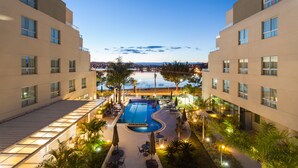 A hotel with a swimming pool, outdoor seating, and a view of the city at dusk. - Esuites Lagoa Santa (Lagoa Santa)