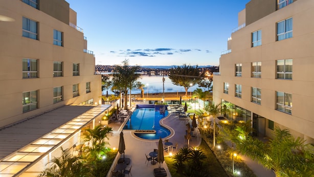 Un hotel con piscina, mobiliario exterior y vistas de la ciudad al anochecer.
