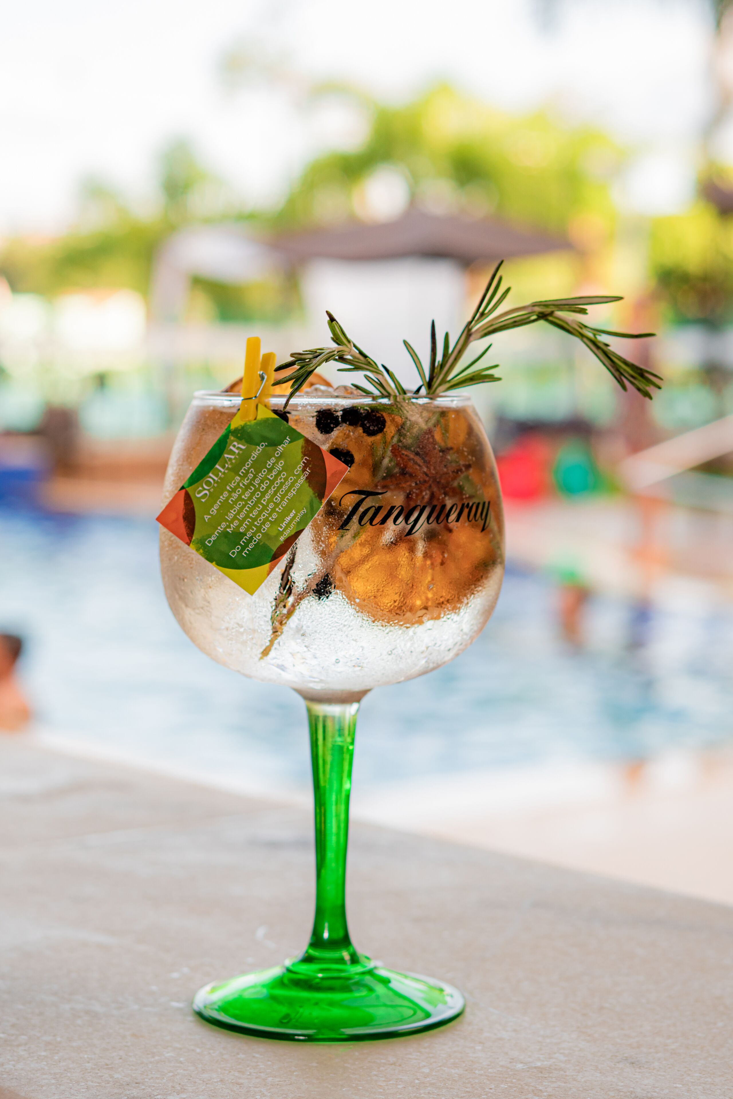 A cocktail glass with a green stem, containing a drink garnished with a sprig of rosemary and a lemon twist, labeled "Tangy."