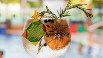 A cocktail glass with a green stem, containing a drink garnished with a sprig of rosemary and a lemon twist, labeled "Tangy."