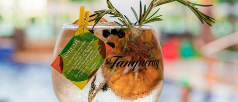 Ein Cocktailglas mit grünem Stiel, gefüllt mit einem Getränk, das mit Rosmarinzweig und Zitronenzeste verziert ist, mit dem Aufdruck "Tangy".