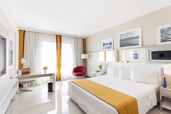 A modern hotel room with a large bed, a desk, a chair, a small table, and a TV.
