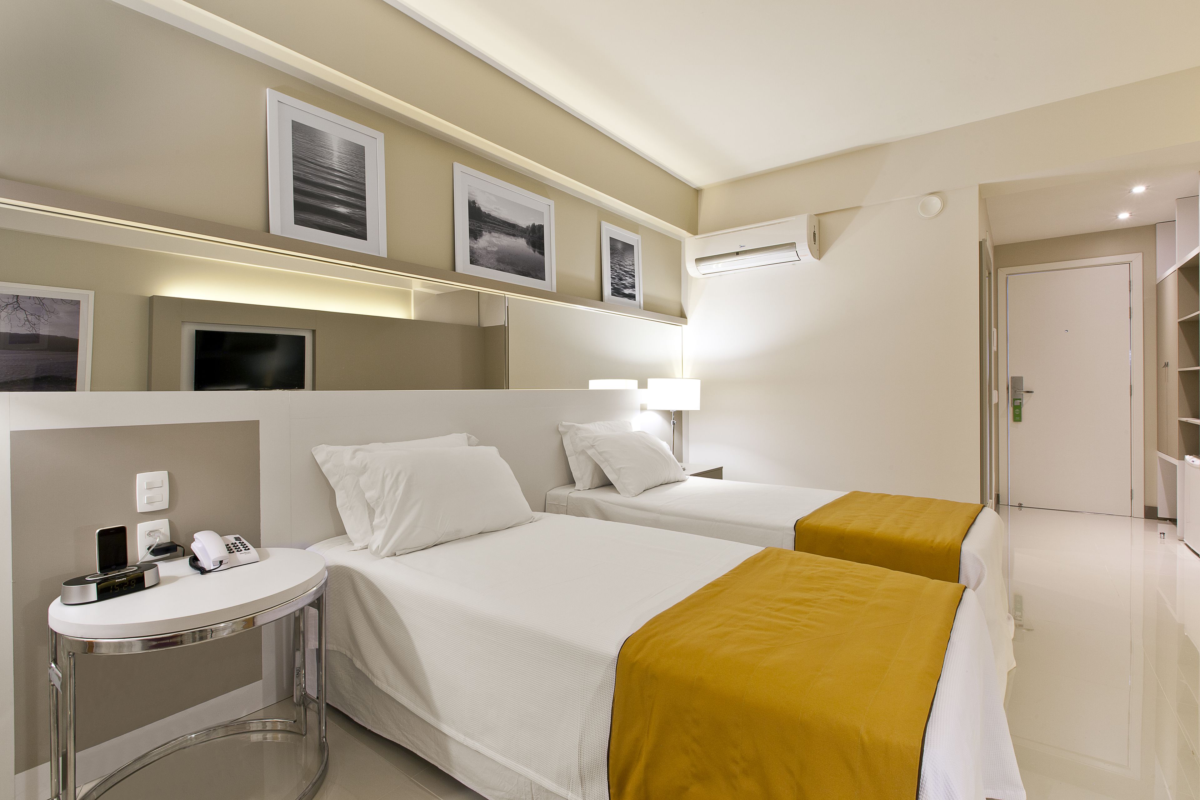 Une chambre d’hôtel avec deux lits, une table de chevet avec un téléphone et une lampe, et un climatiseur fixé au mur.