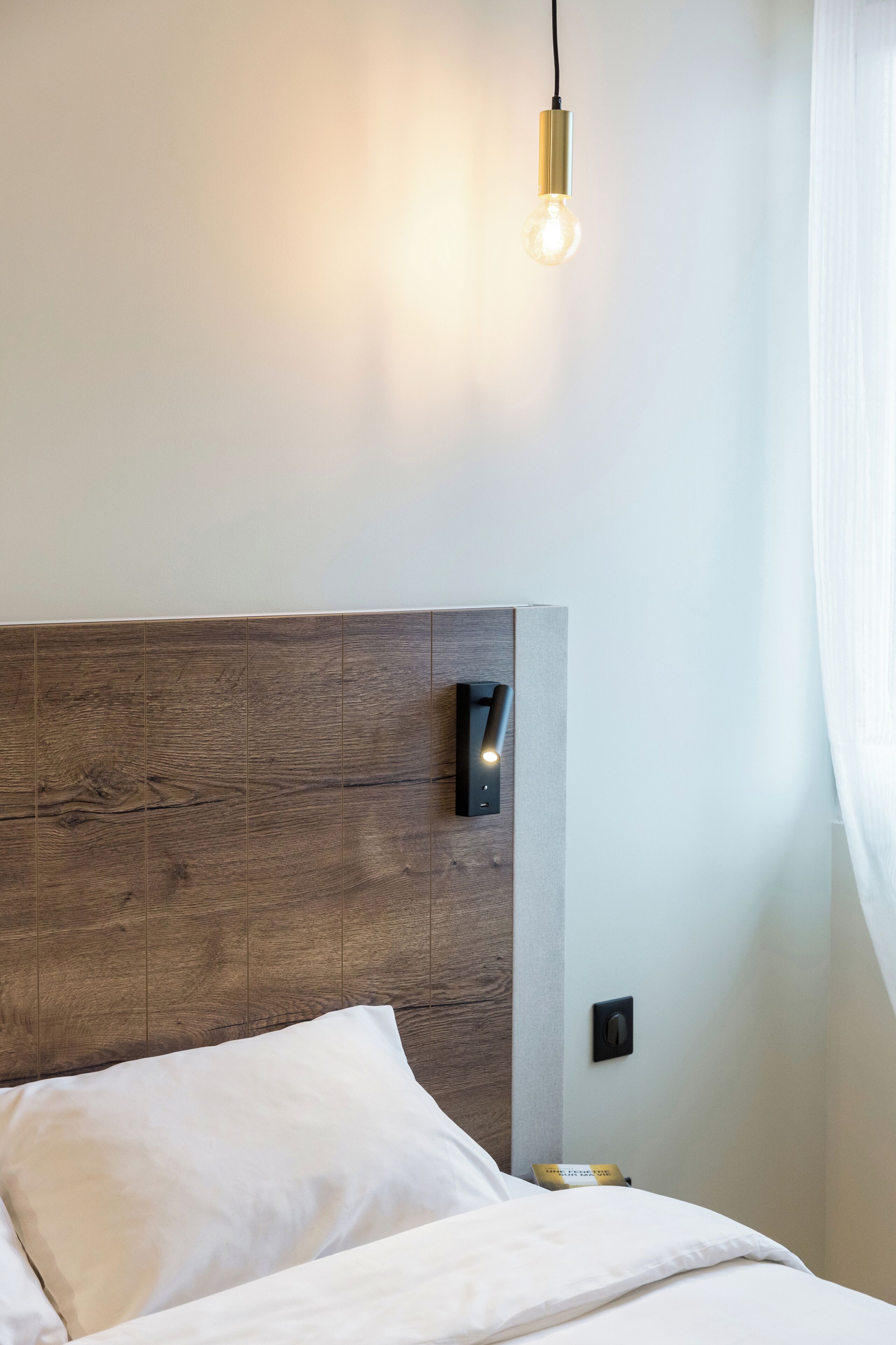 Une chambre à coucher moderne avec une tête de lit en bois, une lampe de chevet et un couvre-lit blanc.