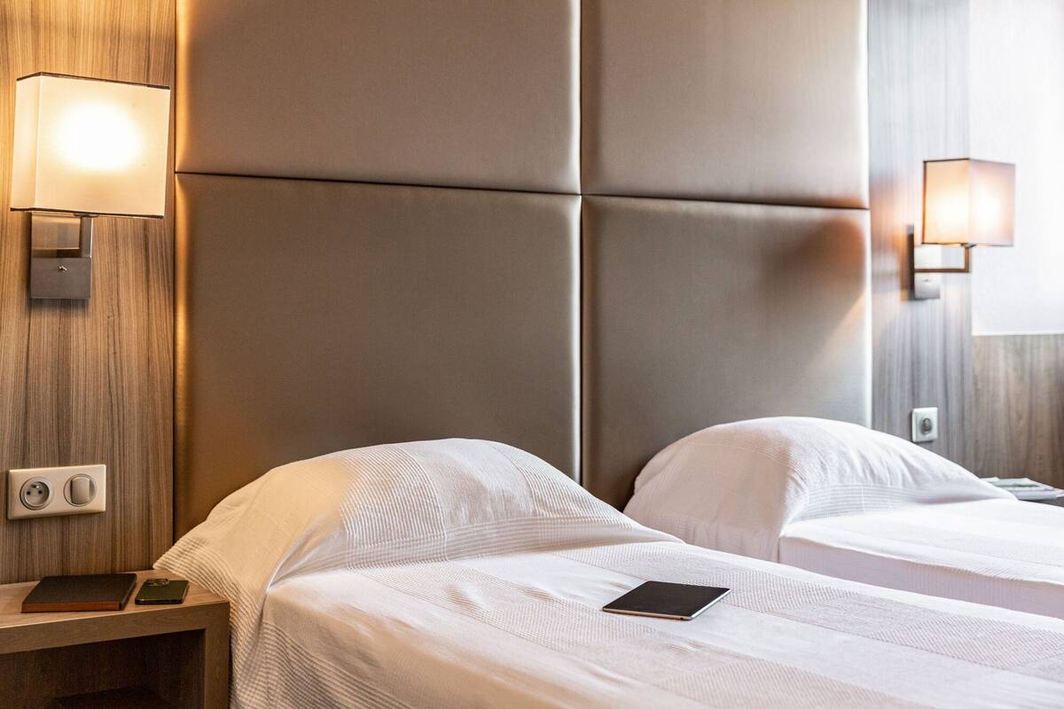 A hotel room with two beds, a nightstand, a lamp, and a wall socket.