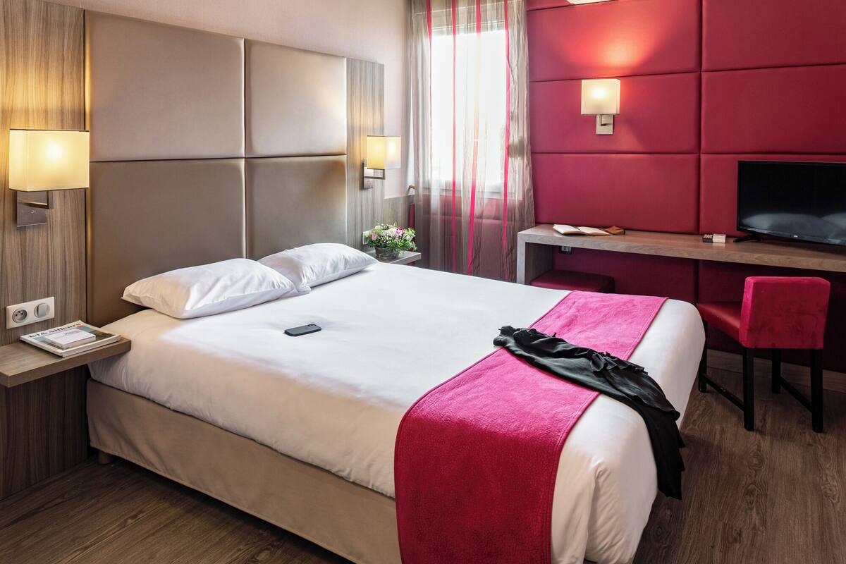 A hotel room with a large bed, bedside tables, a desk, a chair, and a television.