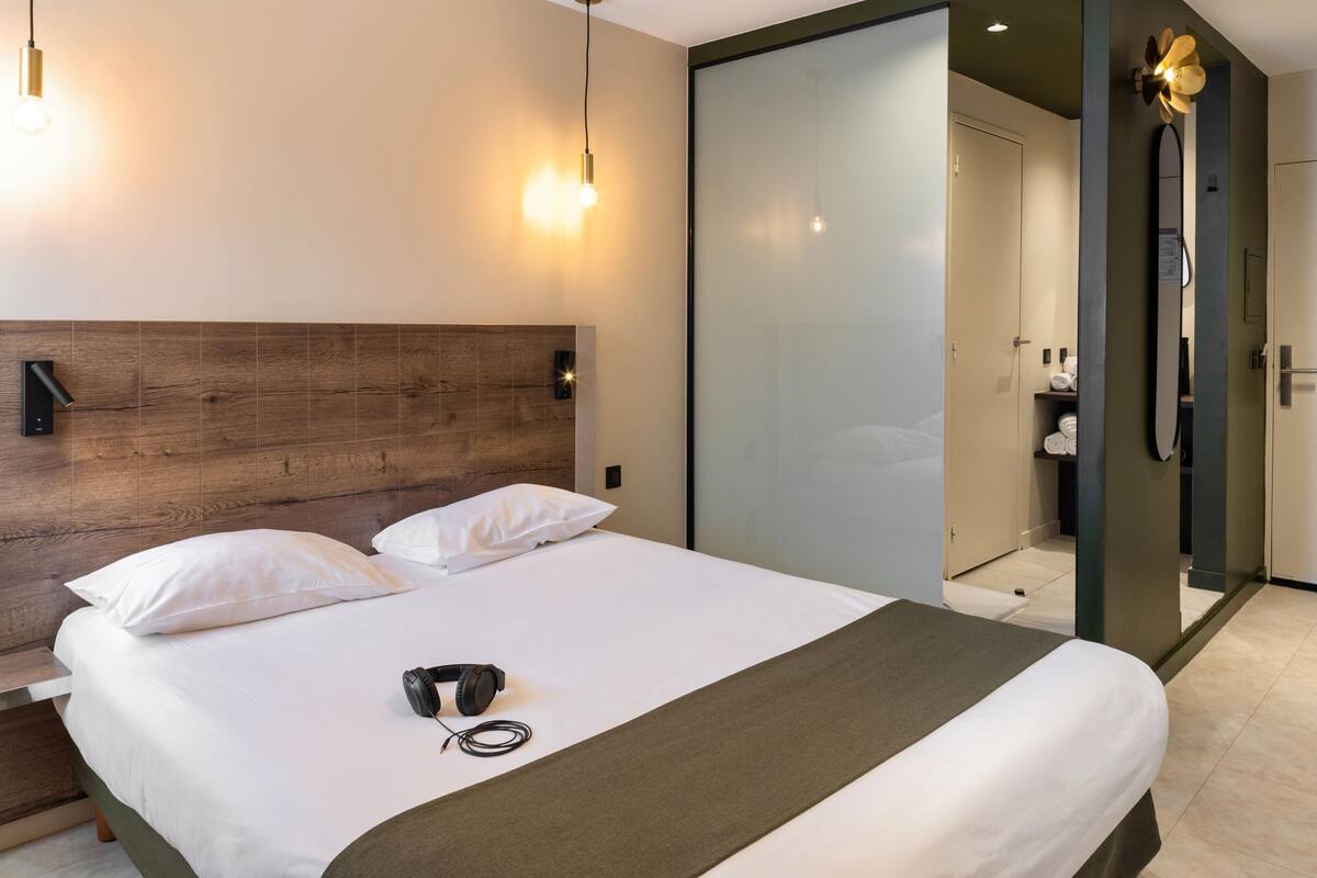 A modern hotel room with a large bed, a wooden headboard, and a glass partition wall.