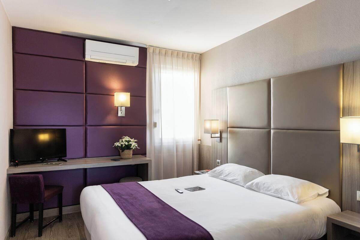 A hotel room with a bed, a desk, a TV, and a window with curtains.