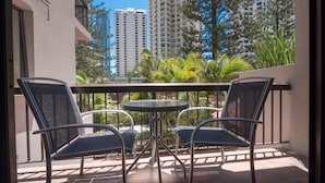 A balcony with two chairs and a small table, overlooking a cityscape with tall buildings and lush greenery. - Trickett Gardens Holiday Inn (Surfers Paradise)