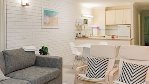 A modern living room with a grey sofa, two armchairs with patterned cushions, a white coffee table, and a dining area with a white table and chairs. - Trickett Gardens Holiday Inn (Surfers Paradise)