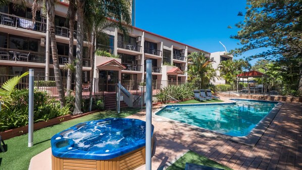 A hotel with a swimming pool, a hot tub, and a covered outdoor area with lounge chairs.