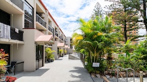 A multi-story hotel with balconies, outdoor seating, and lush greenery. - Trickett Gardens Holiday Inn (Surfers Paradise)