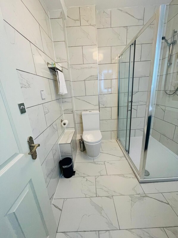 Un baño con inodoro, cabina de ducha de vidrio y cubo de basura.