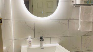 A bathroom with a white sink, a mirror with a light, and a towel rack. - Euro Bar and Hotel (Oxford)